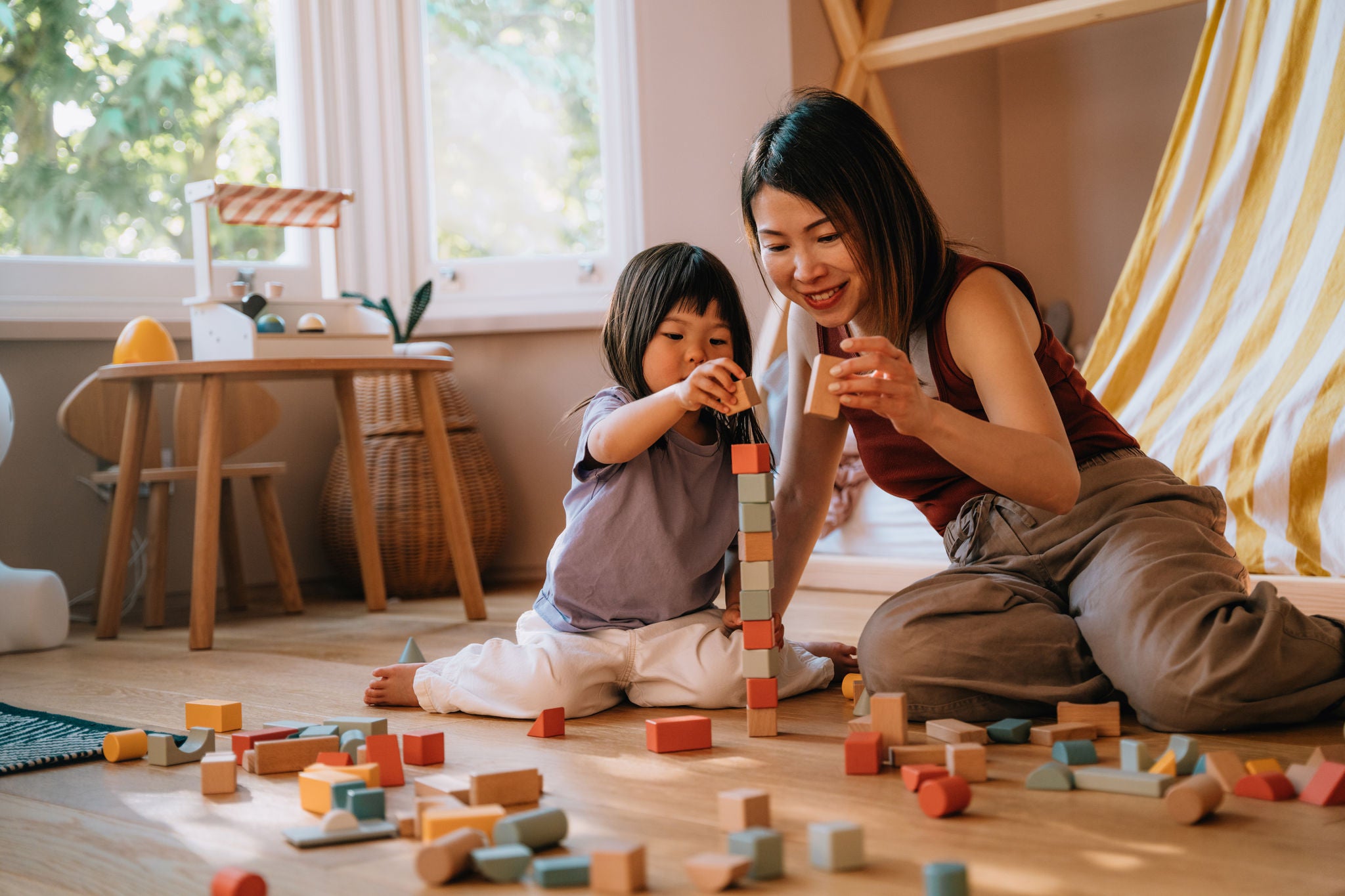 Young Asian mother and her little girl having fun, playing with toys together in the bedroom. Family love and togetherness. Children earning through play.